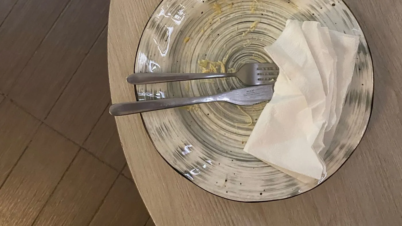 Tom tallrik med kniv, gaffel och skrynklad servett på ett runt träbord, sedd rakt uppifrån.