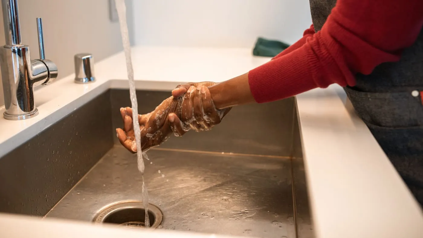 Händer som tvålas in under rinnande vatten i en rostfri diskho.