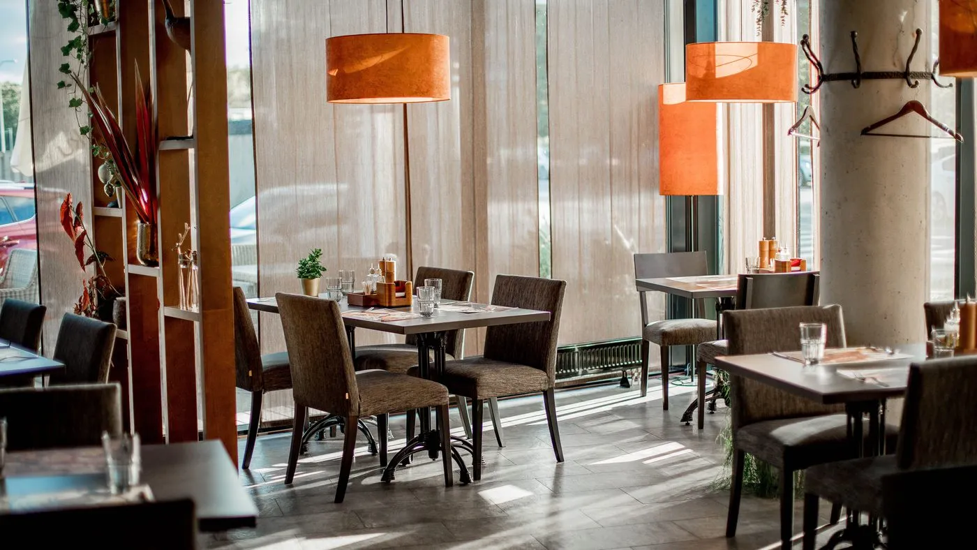 Tom restaurangsal med dukade bord, trästolar och pendellampor i varmt ljus.